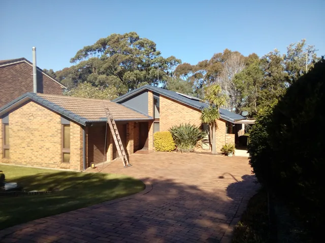 Brick house with a dull, patchy tile roof and a ladder against the gutter, before restoration.