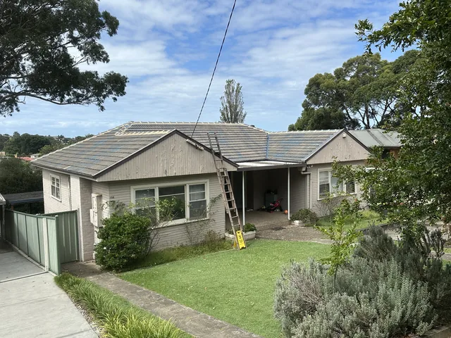 Rendered house with a faded pale grey tile roof and a ladder against the gutter, before restoration.