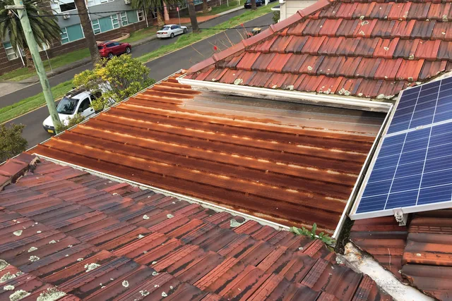 Rusted metal skillion roof beside terracotta tiles covered in lichen.