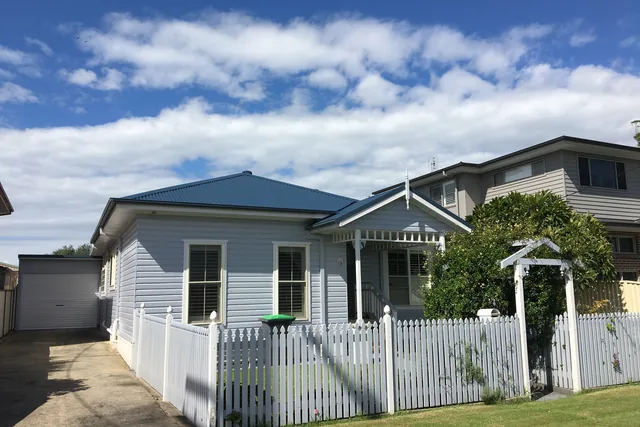 Weatherboard cottage with a restored deep navy metal roof and a white picket fence.