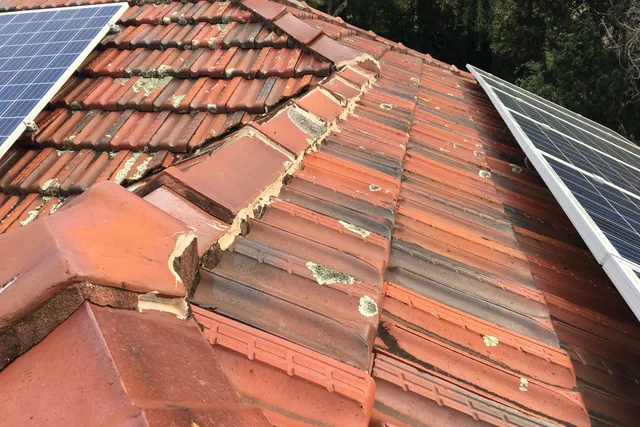 Broken and displaced ridge caps with crumbling mortar on a terracotta tile roof.