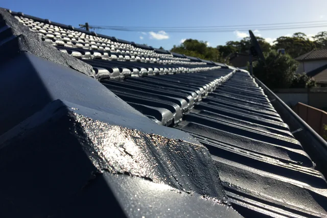 Freshly coated charcoal tile roof, still wet, with new ridge pointing.
