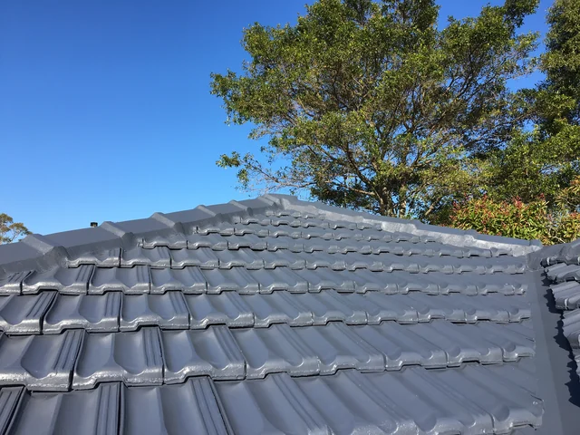 Restored charcoal tile roof with new ridge and hip lines against a blue sky.