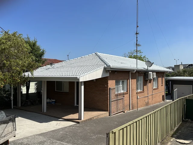 Brick home with a freshly coated pale grey tile hip roof and a carport.
