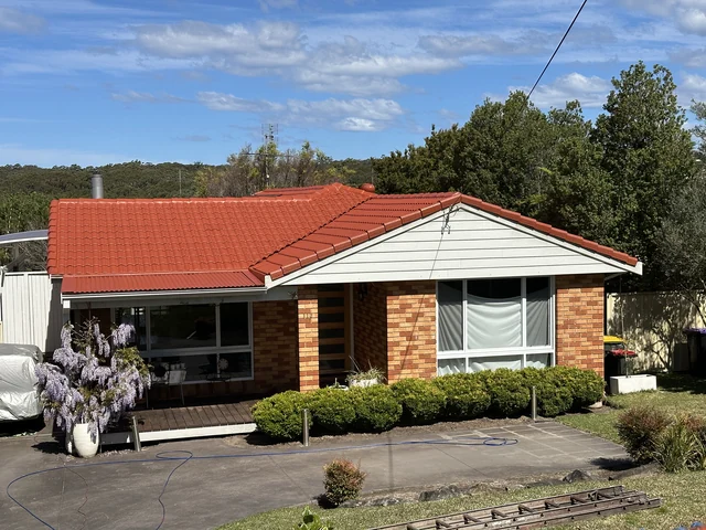 Brick house with a restored bright red tile roof and wisteria in bloom.