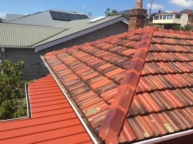 Restored terracotta tiles with new ridge capping beside a grey metal roof and a brick chimney.