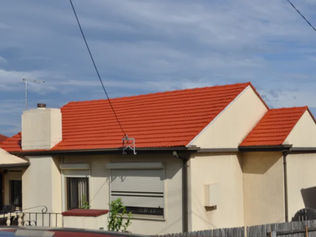 Cream rendered house from the street with a restored terracotta tile roof and two gable ends.